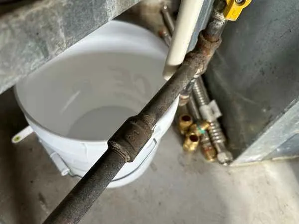 White bucket placed under the end of a water heater relief valve discharge pipe